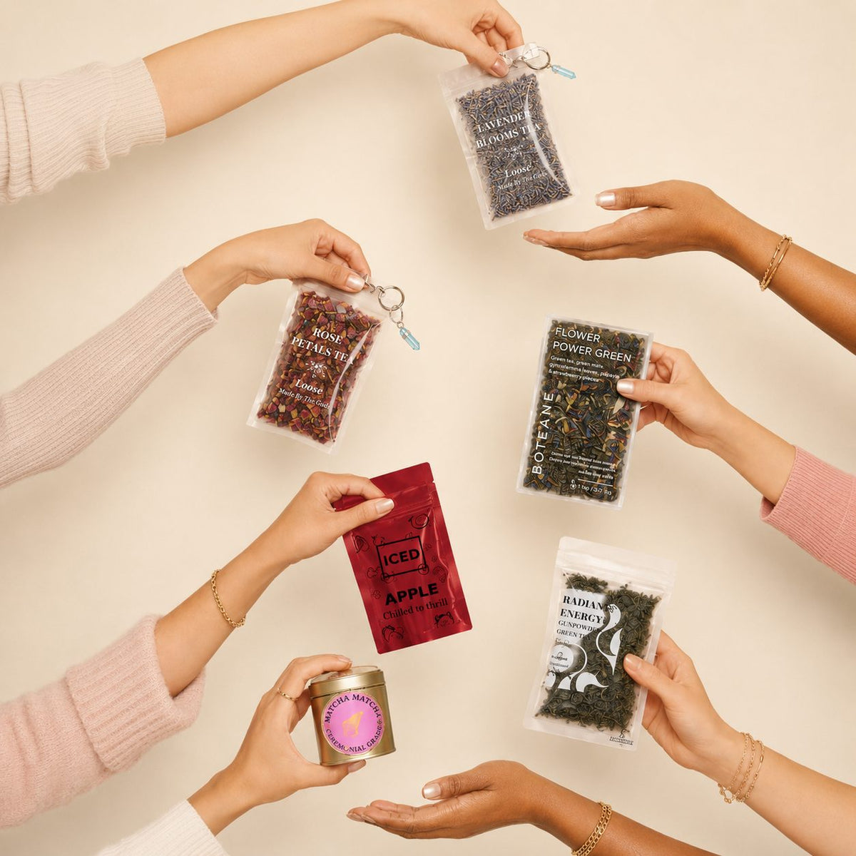 Six hands reaching in from the edges of the frame, each holding a different Boteane loose-leaf tea pouch or tin, on a warm cream background