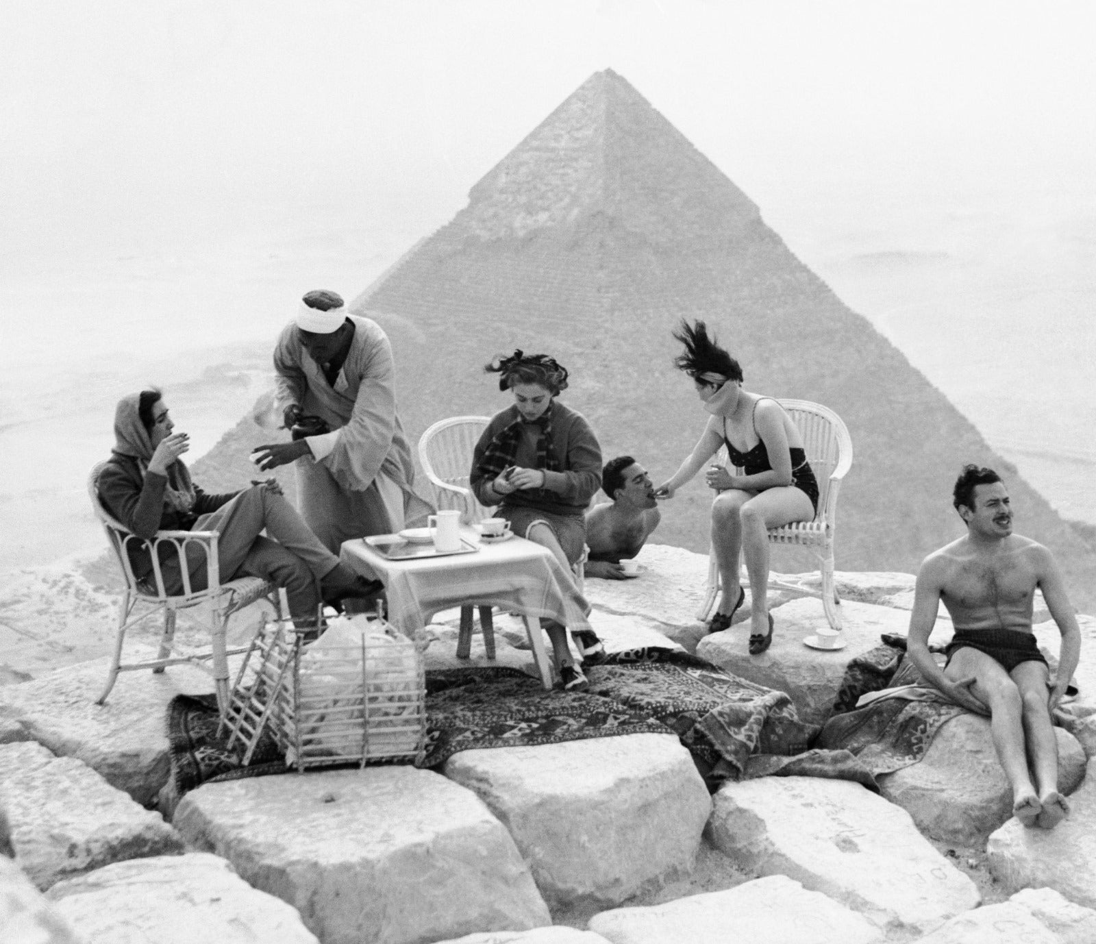 Black and white photograph of people taking tea at a small table in front of a pyramid
