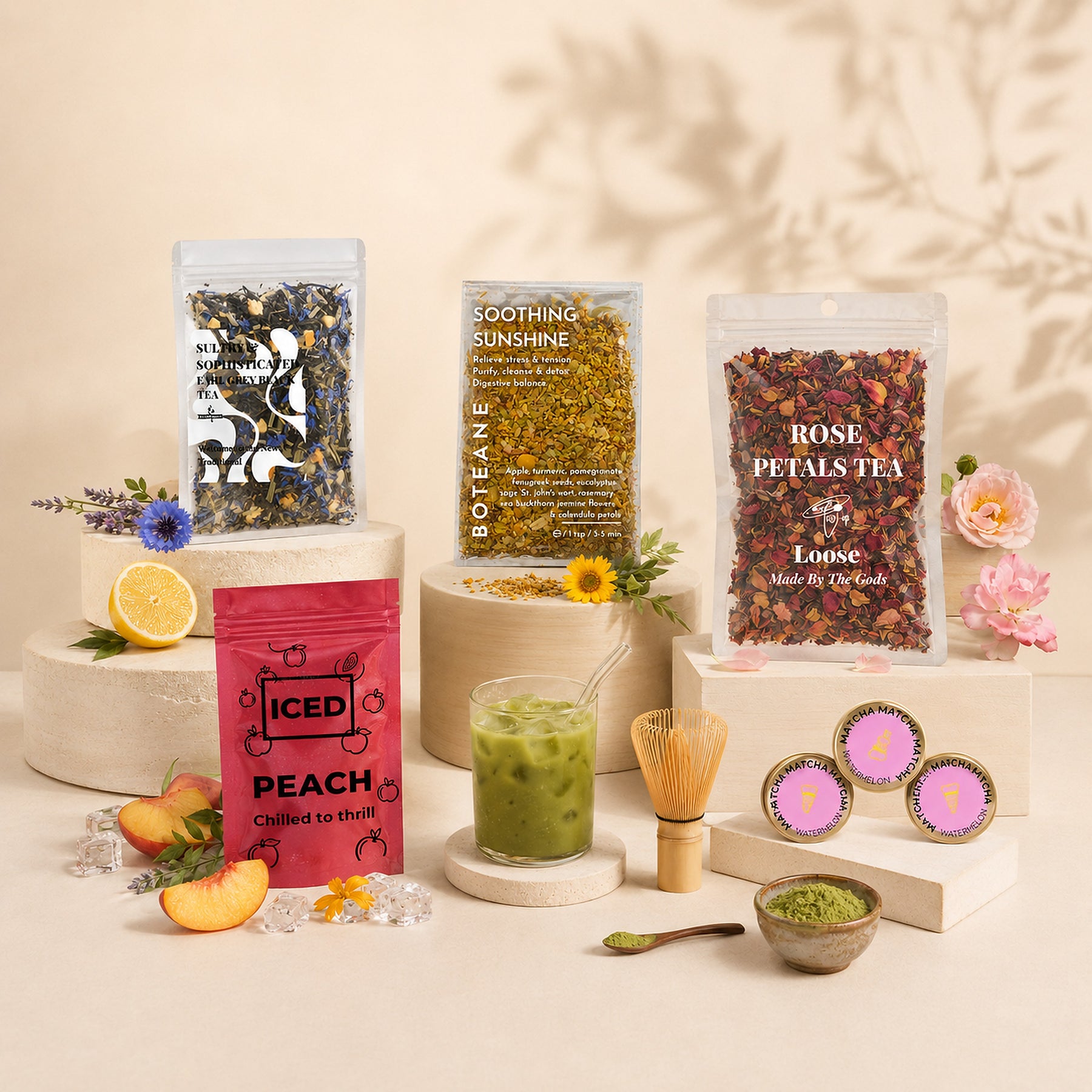A styled display of Boteane teas on cream pedestals: pouches of loose tea, an Iced Peach bag, a green iced tea, matcha and a bamboo whisk