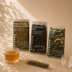 Three Boteane tea packages on a beige surface with a cup of tea and a glass.