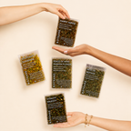 Hands holding Botane tea packages on a beige background