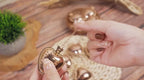 Heart-shaped pendant held by a hand with a wooden surface and plant in the background