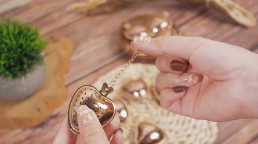 Heart-shaped pendant held by a hand with a wooden surface and plant in the background