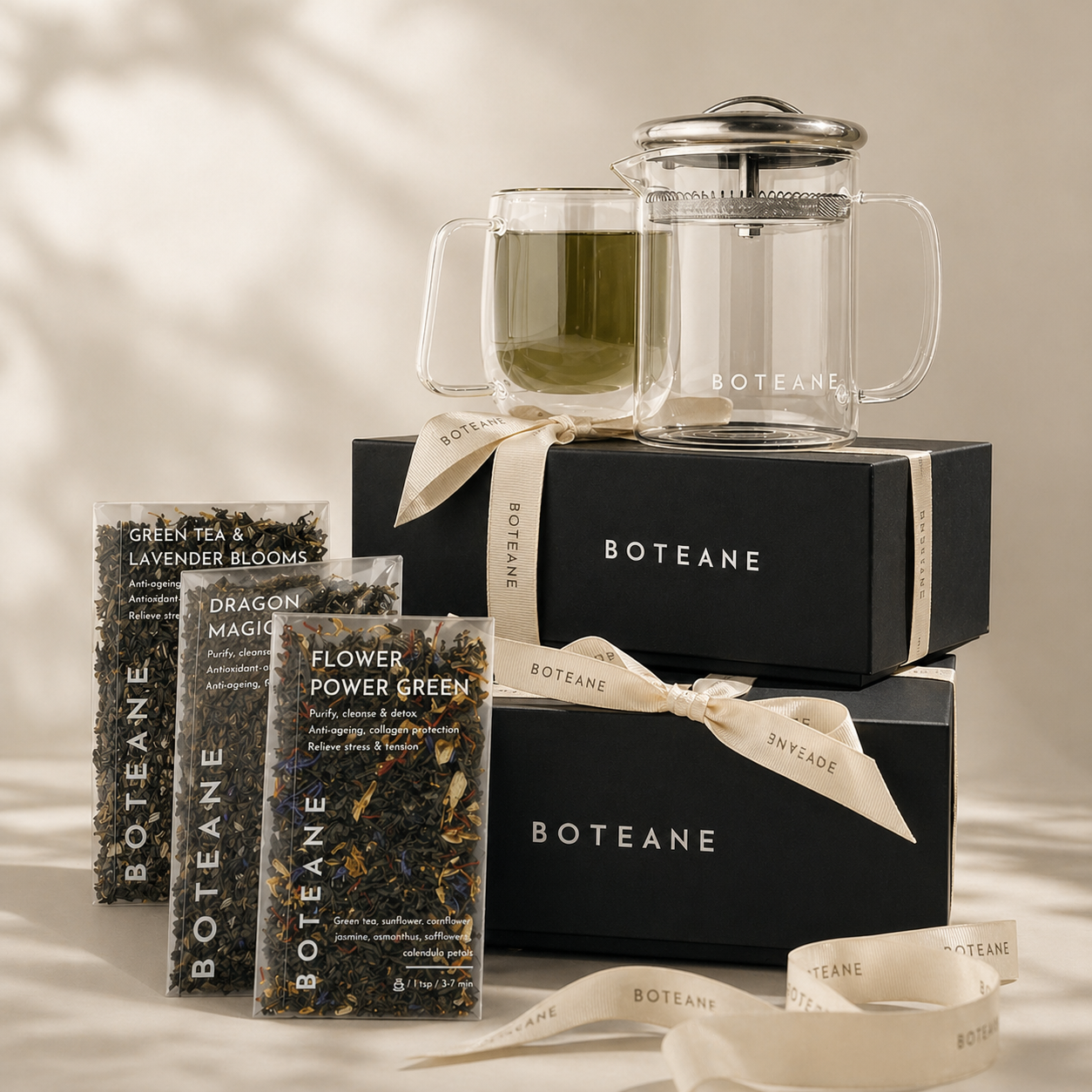 Boteane tea set with glass teapot, black boxes, and tea bags on a neutral background